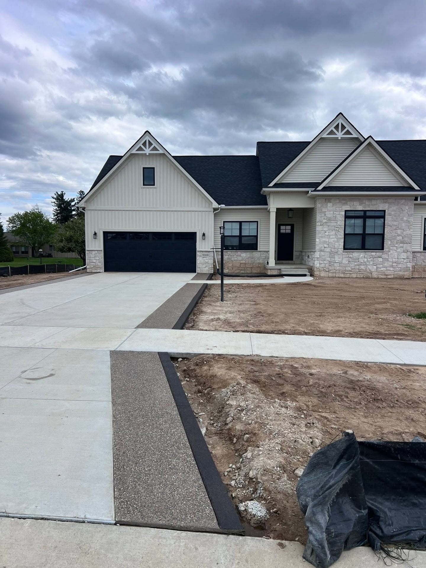 New construction home with exposed aggregate concrete driveway and dark accent border