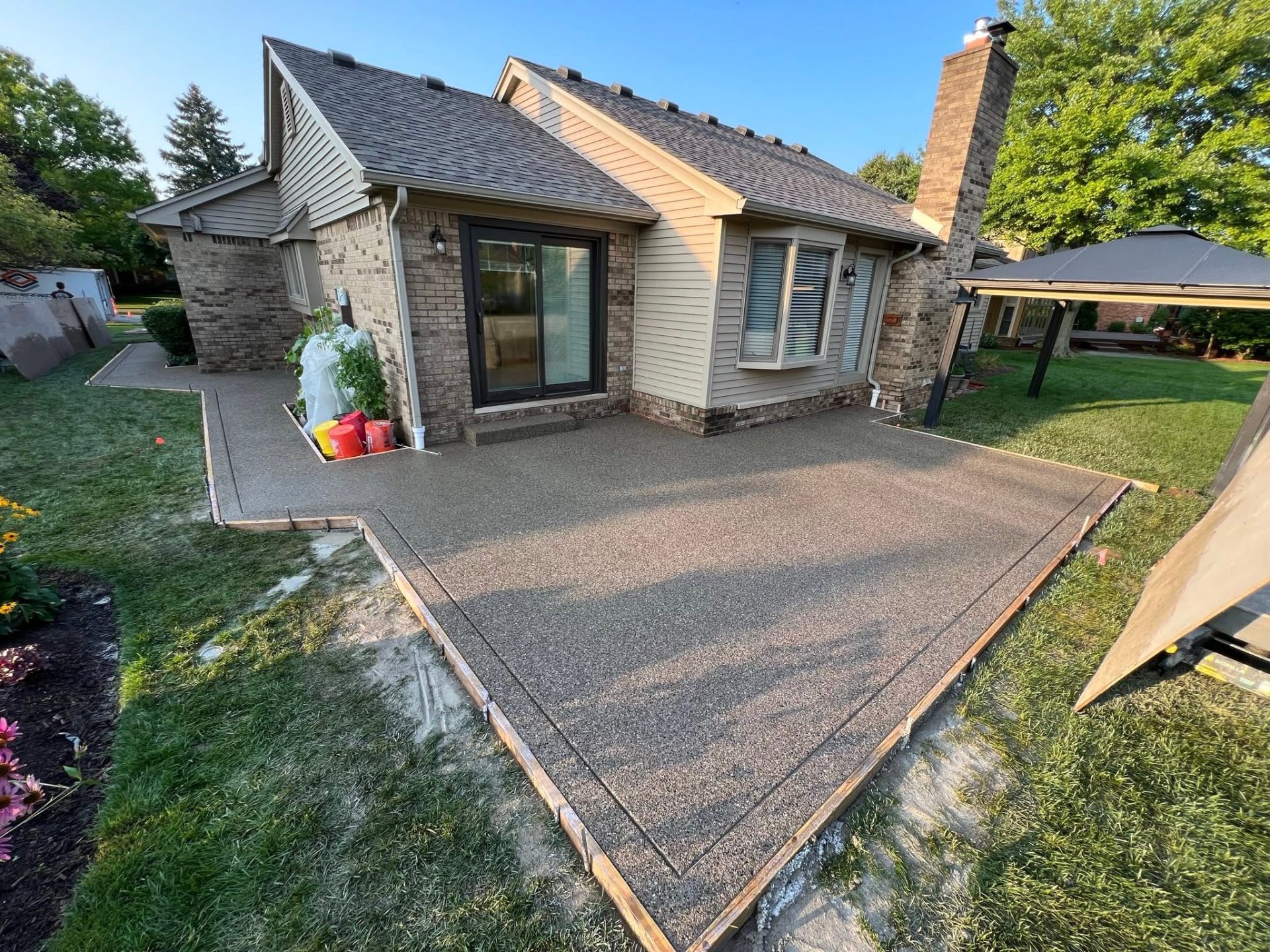 Freshly poured exposed aggregate backyard patio with wood forms beside a brick home