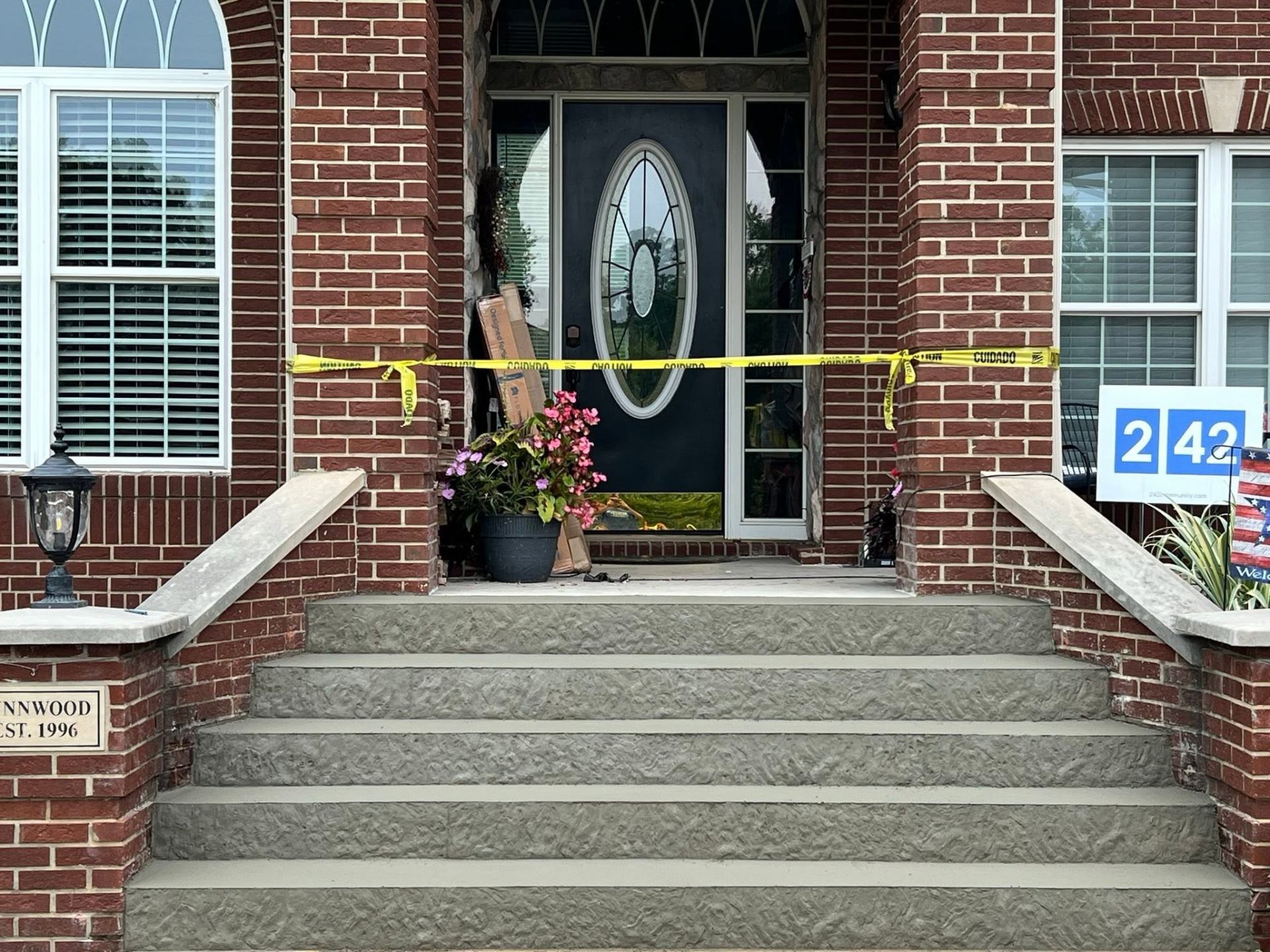 Brick home front entry with textured concrete steps, matching railings, and potted flowers