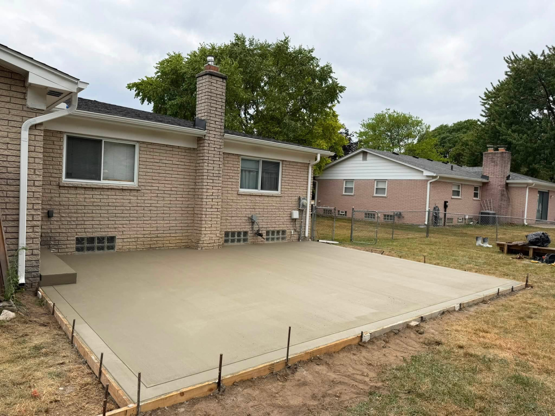 Freshly poured broom-finished concrete patio behind a brick ranch home