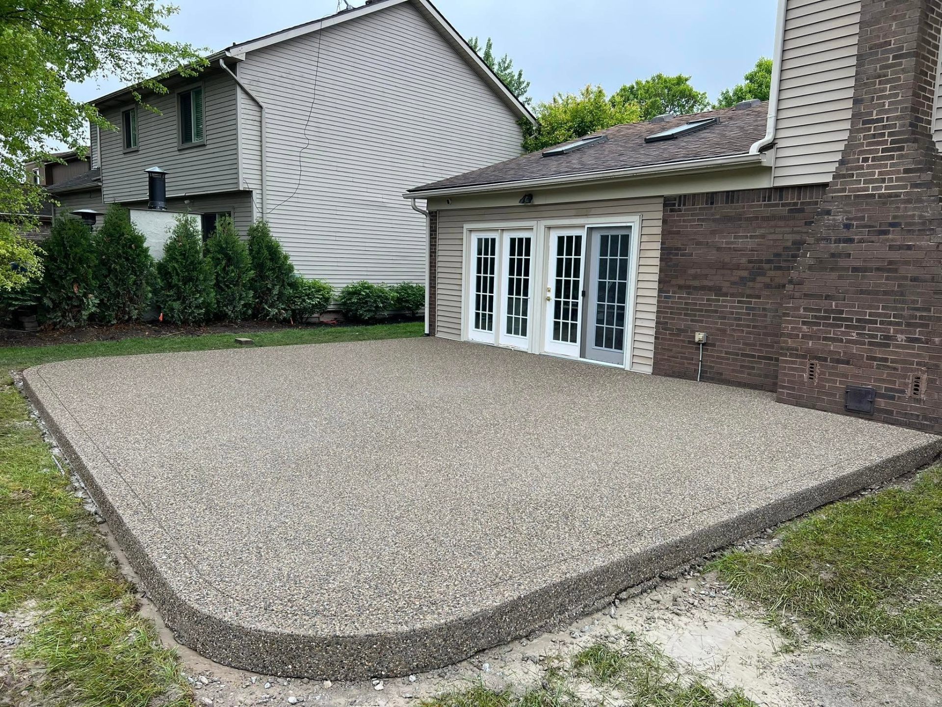 Exposed aggregate patio at rear of brick home with French doors