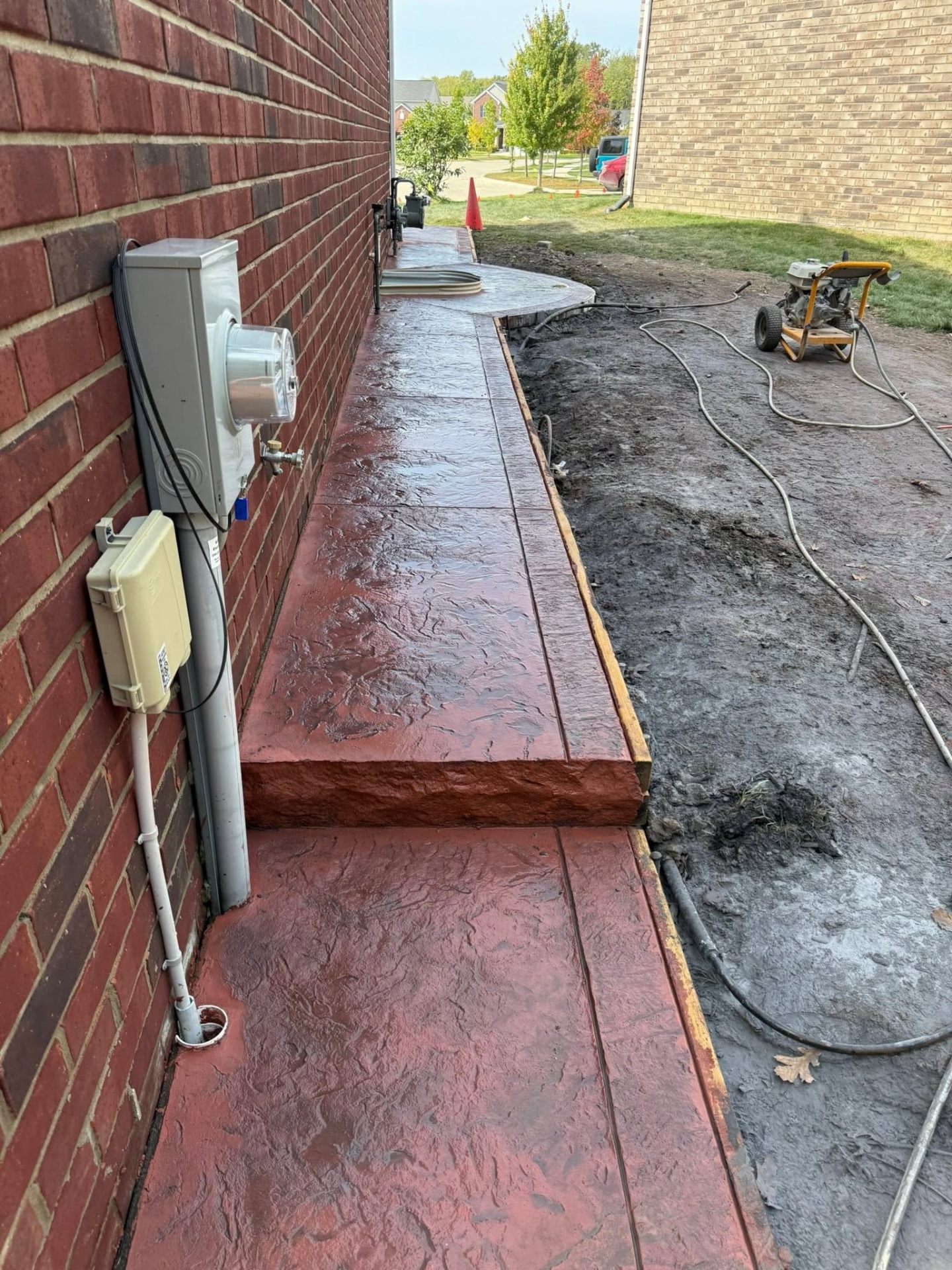 Red stamped concrete walkway along side of brick house