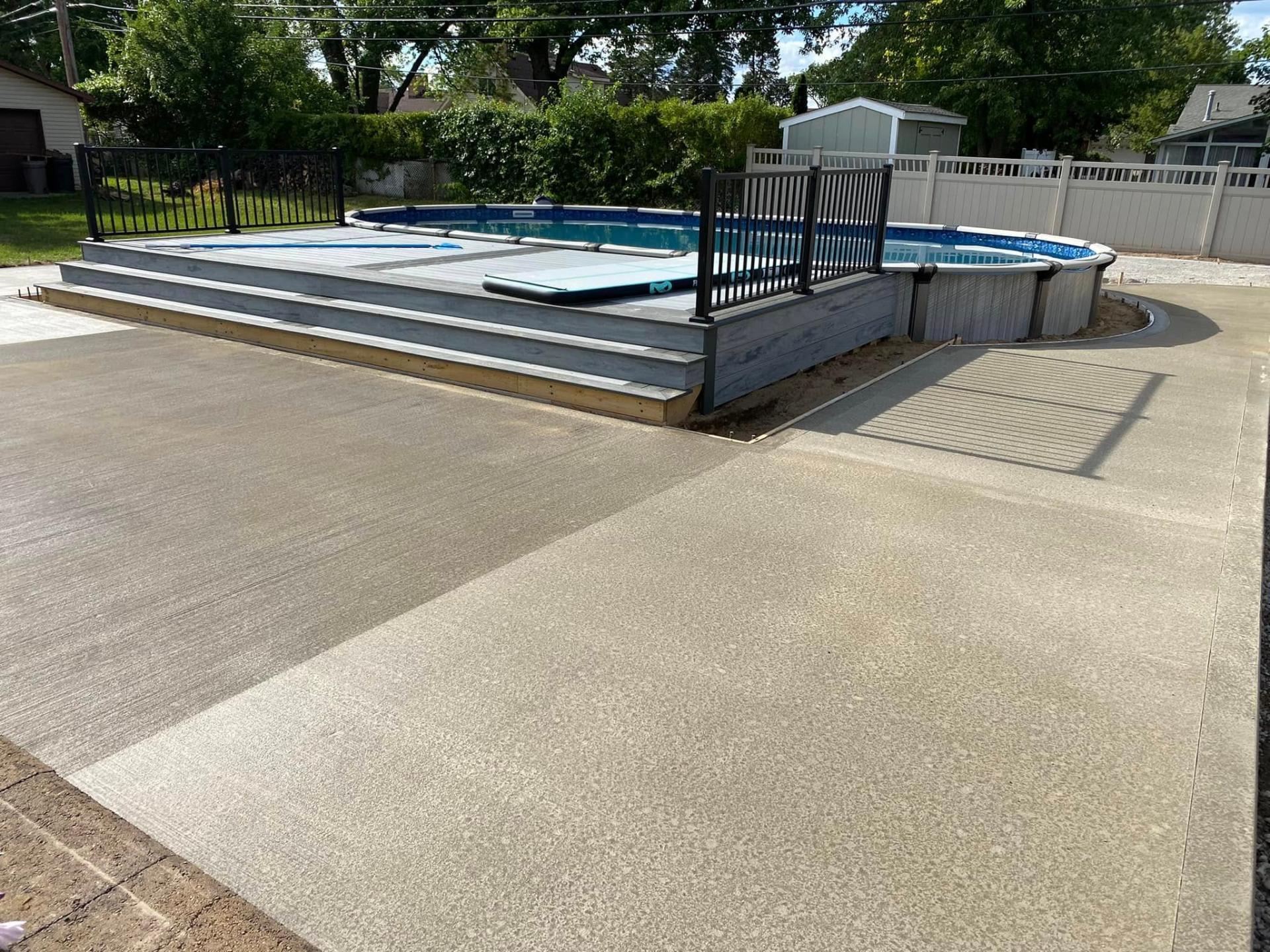 Exposed aggregate concrete deck surrounding above-ground pool with raised wood platform