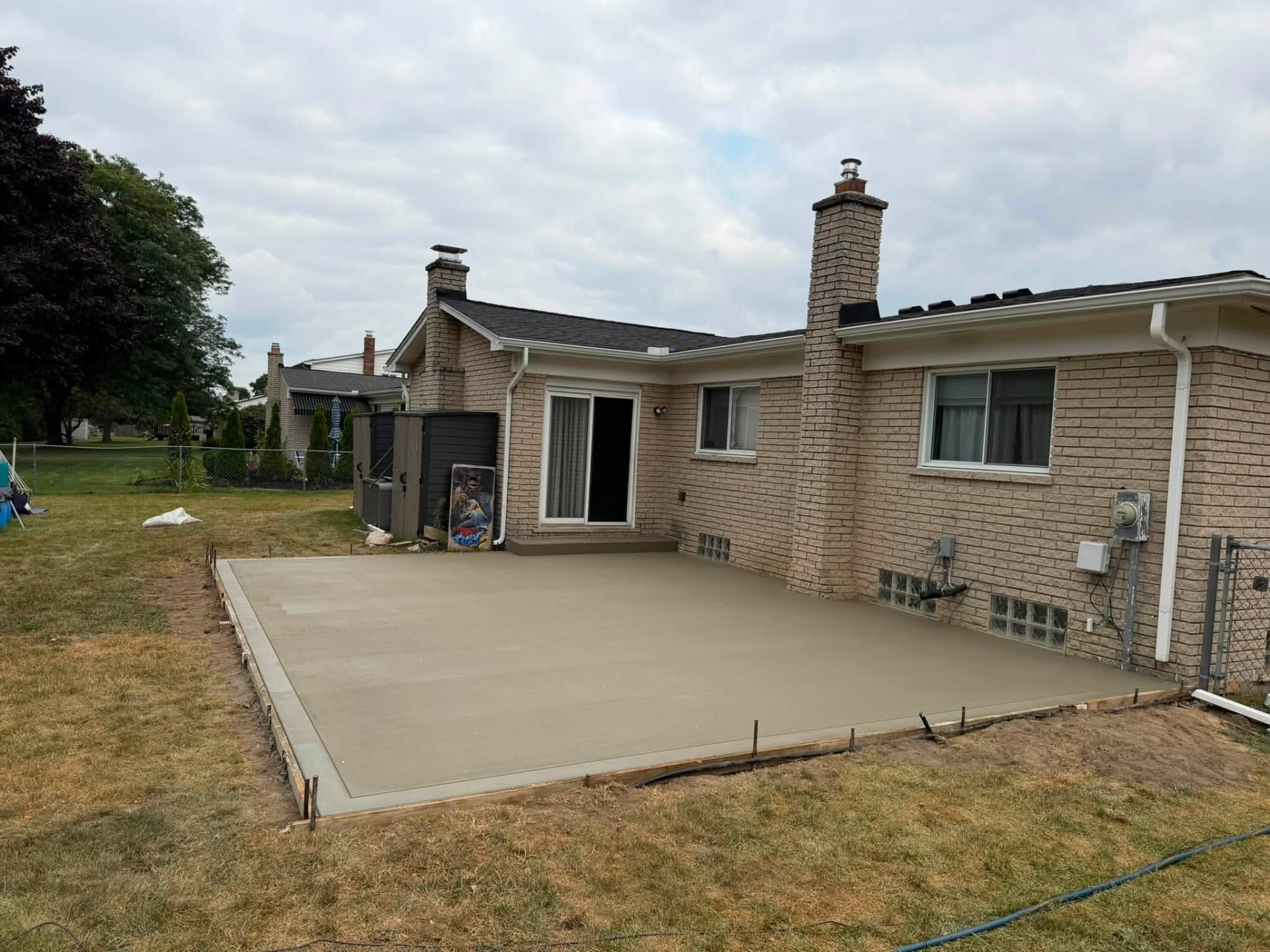 Wide freshly poured concrete patio spanning the rear of a brick home
