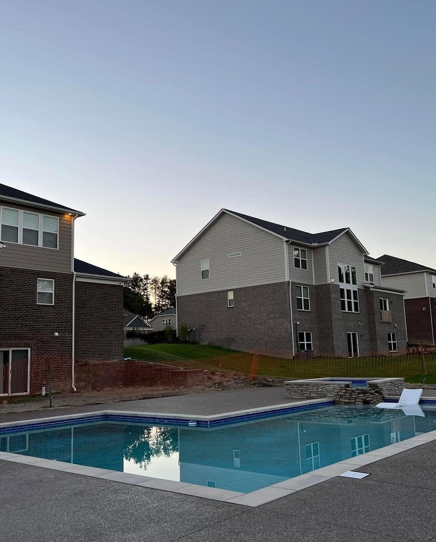 In-ground pool with spillover spa and exposed aggregate deck at dusk